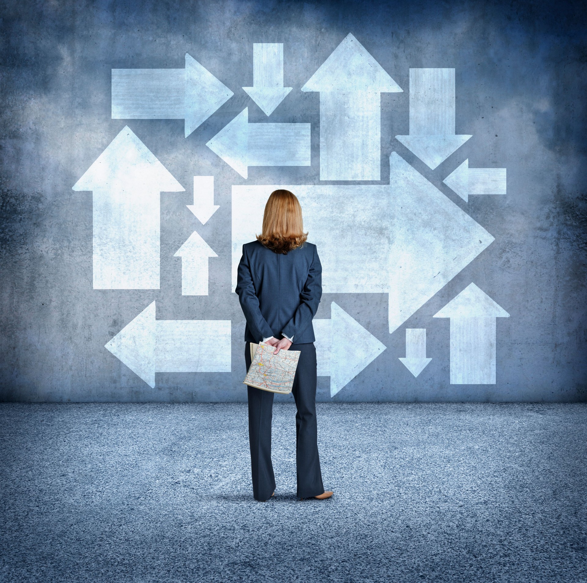 Businesswoman Looking Up At Large Arrows While Holding Road Map In Her Hands
